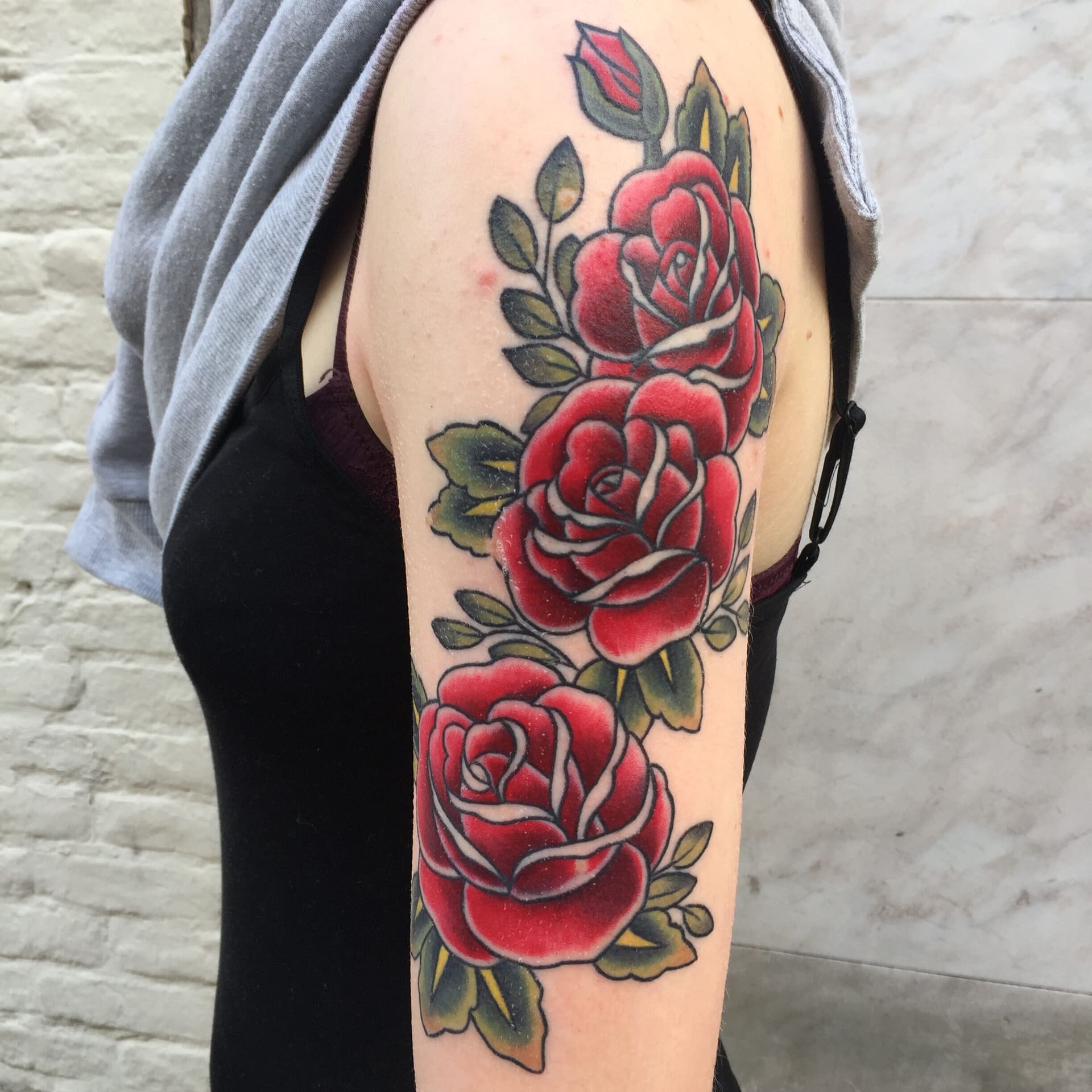 Drie rode rozen met groene bladeren in old school stijl op een bovenarm.